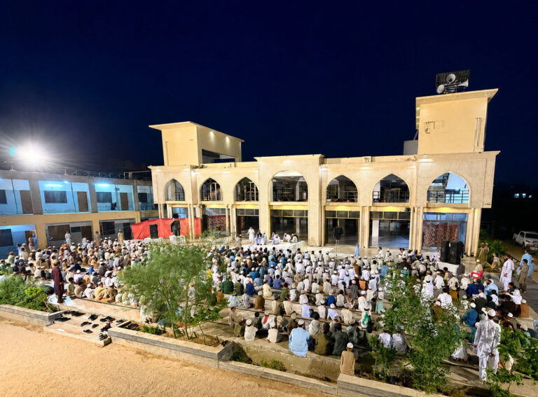 An evening gathering in front of the illuminated arched building at Jamia Baitul Ateeq.